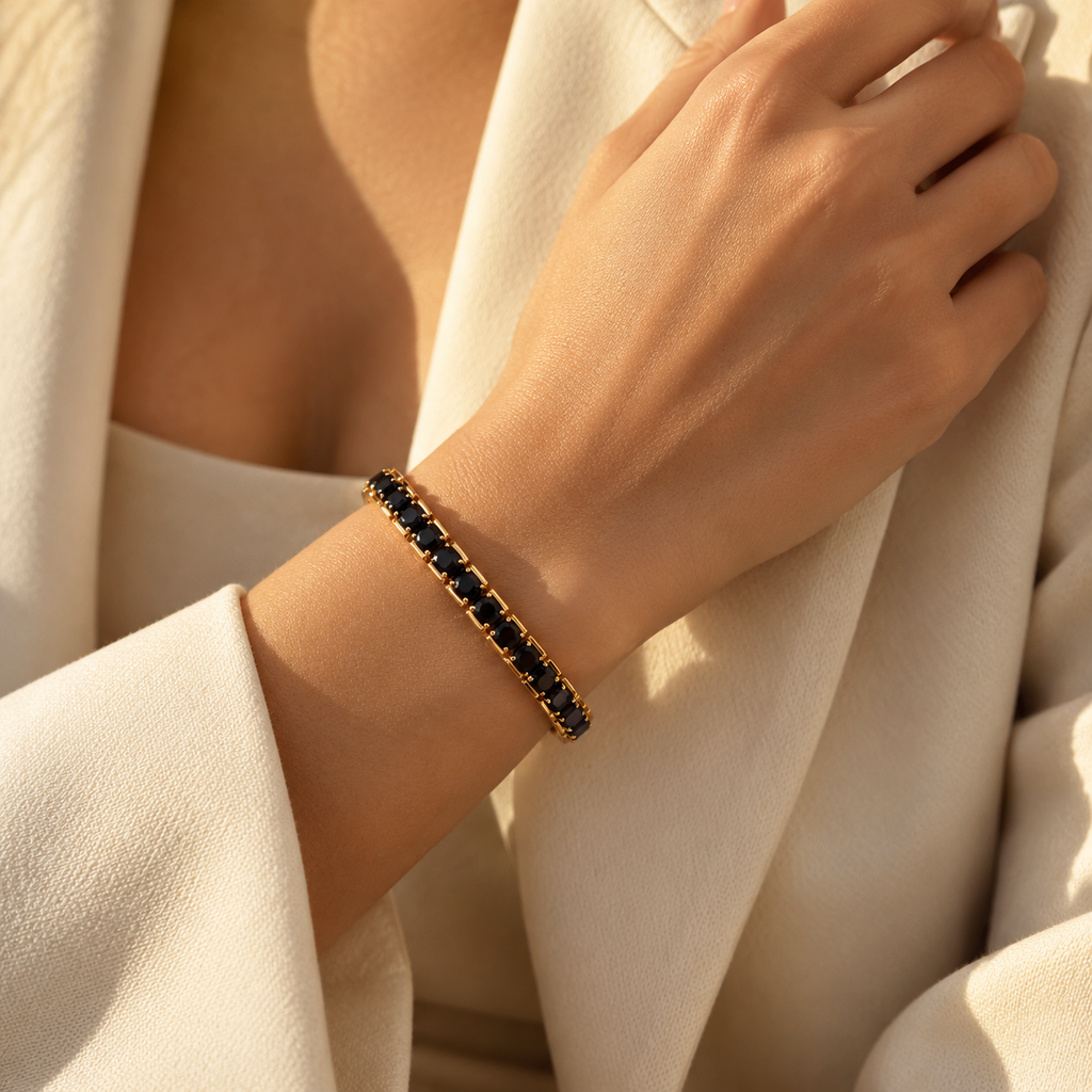 Close-up of a woman's wrist wearing the black zircon gold stretch tennis bracelet paired with a tailored white blazer.
