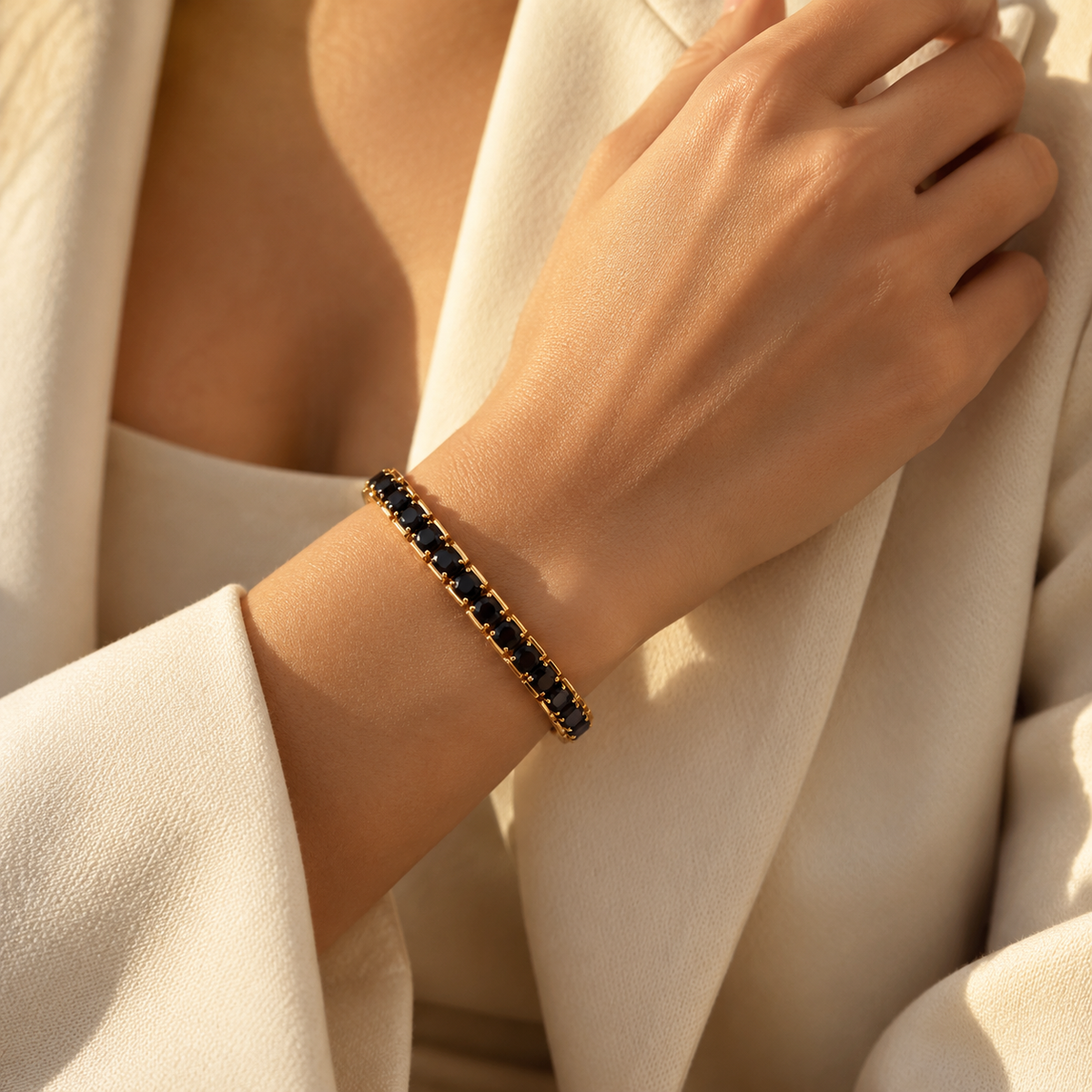 Close-up of a woman's wrist wearing the black zircon gold stretch tennis bracelet paired with a tailored white blazer.
