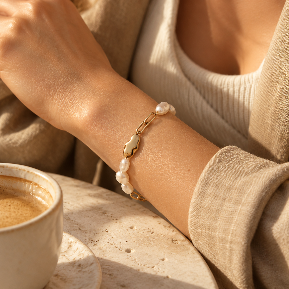 Close-up of woman wearing half pearl half gold paperclip chain bracelet with cozy knitwear
