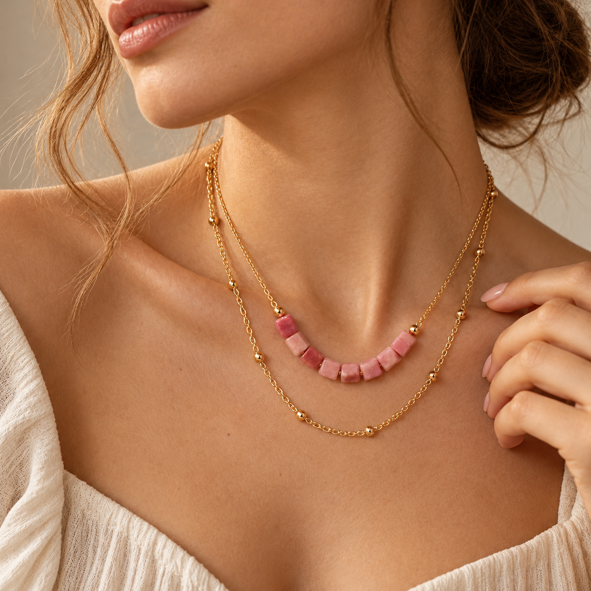 Close-up neckline view of a woman wearing the double-strand pink cube bead bar and gold bead chain necklace.
