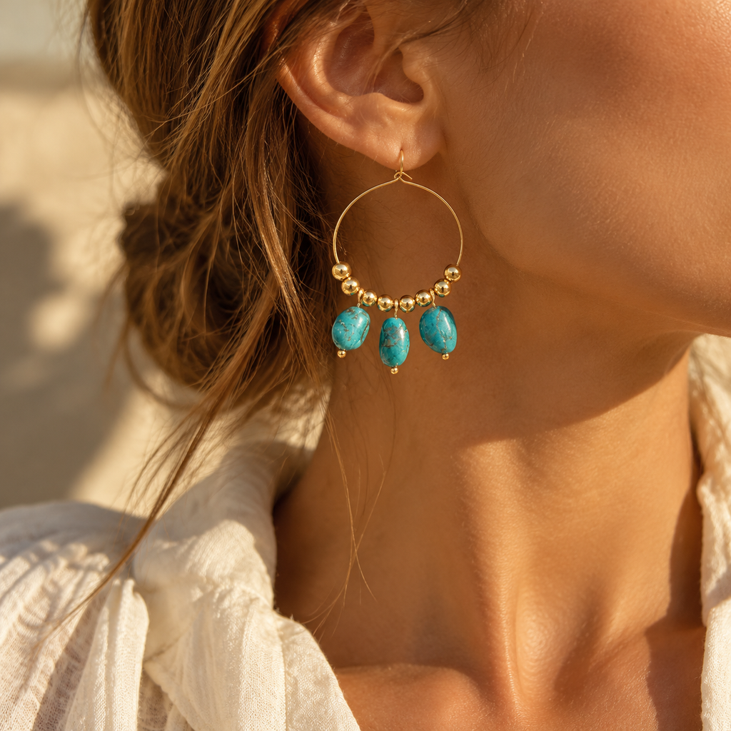 Detailed close-up shot of model ear showcasing large gold hoop earring with three dangling turquoise pebble charms

