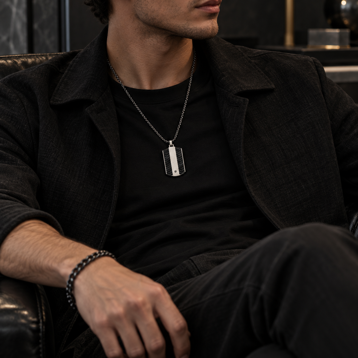 Model sitting in leather armchair wearing men's steel dog tag necklace
