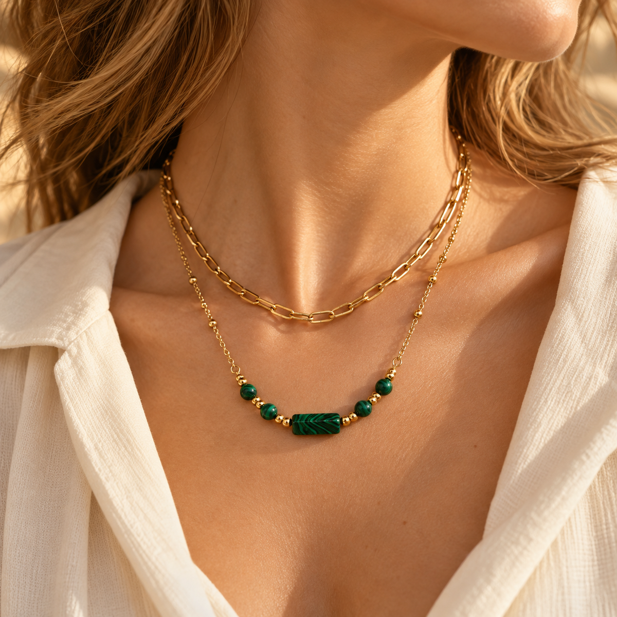 Side angle neckline shot showing the elegant layered green malachite stone bar and gold link chain necklace in warm sunlight.
