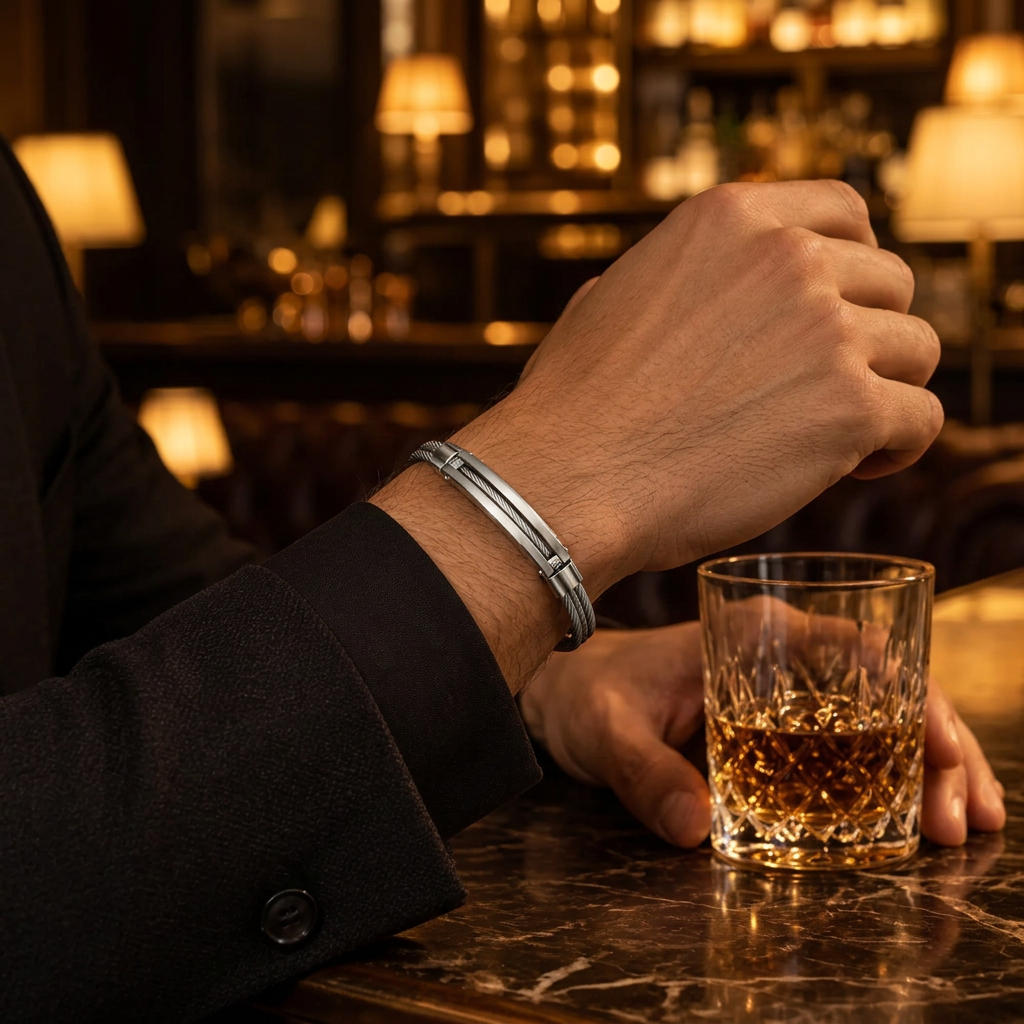 Close-up wrist view of men's all-silver cable bangle bracelet on marble bar table
