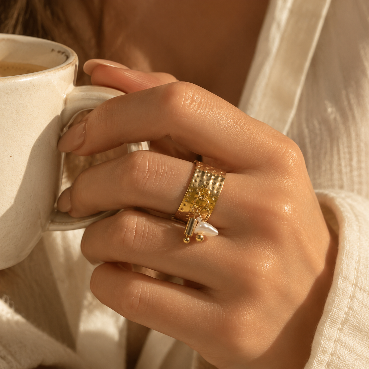 Lifestyle photo of woman wearing hammered gold pearl dangle ring while holding coffee cup
