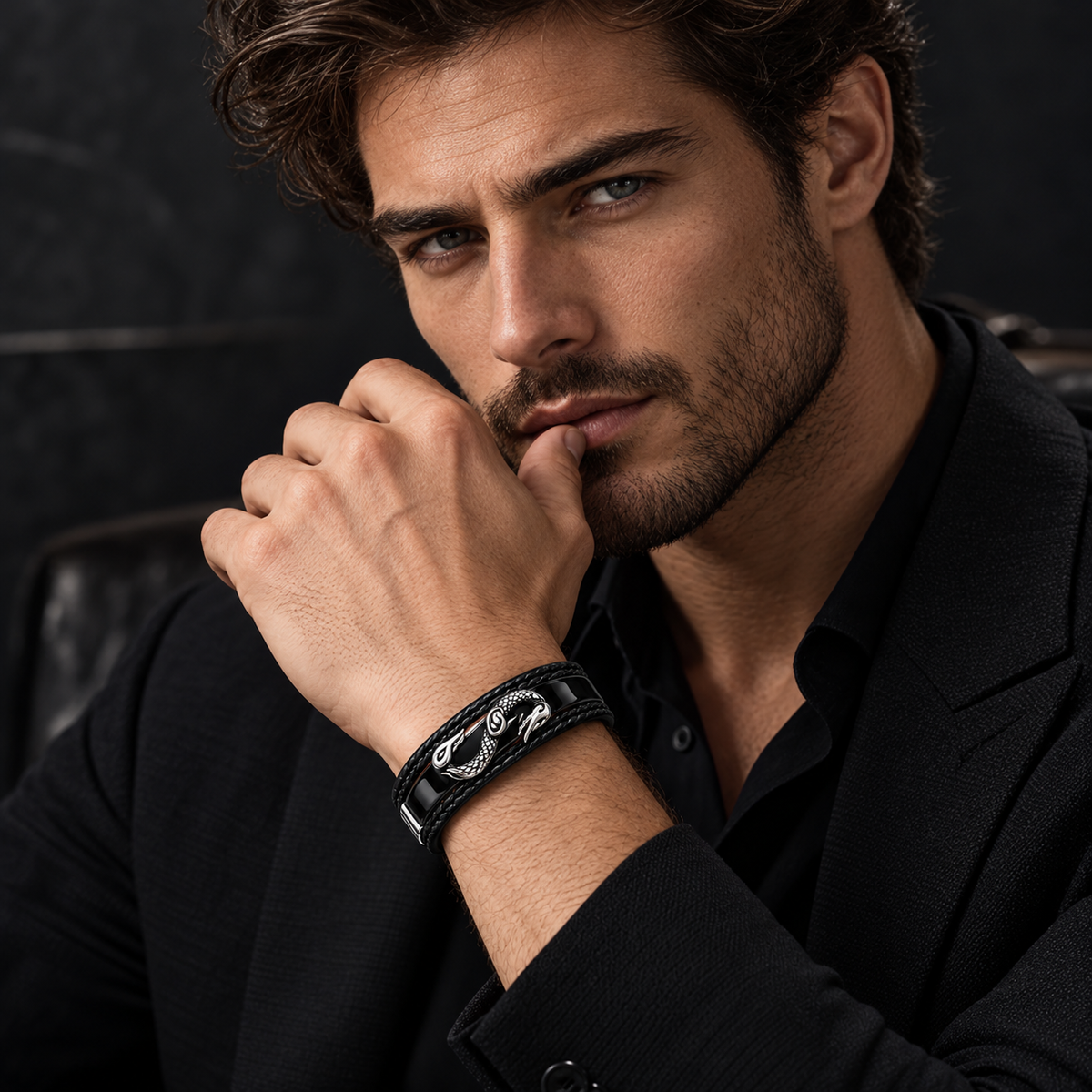 Close-up portrait of handsome male model in all-black suit wearing dragon bracelet

