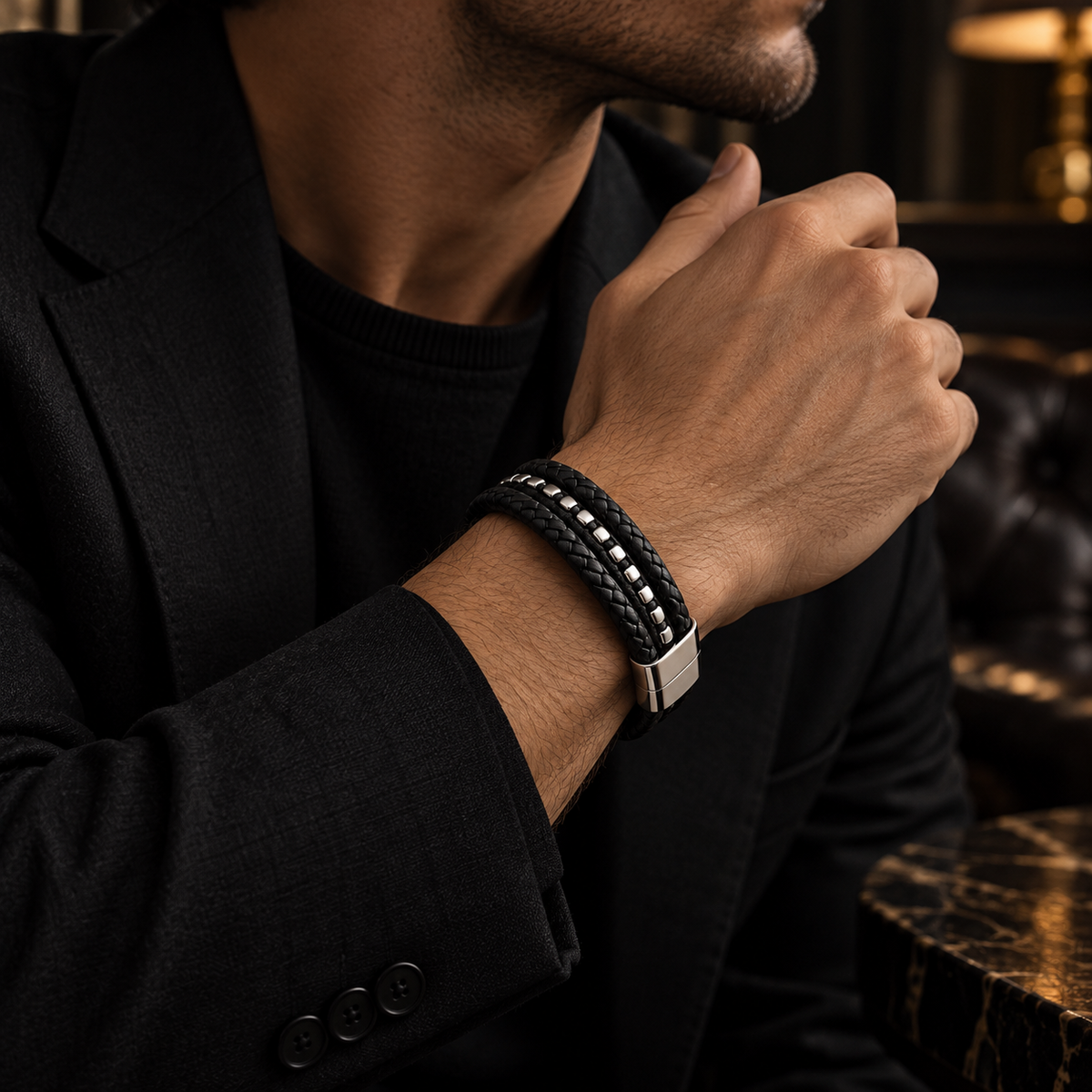 Male wrist wearing black braided leather studded bracelet with tailored black blazer
