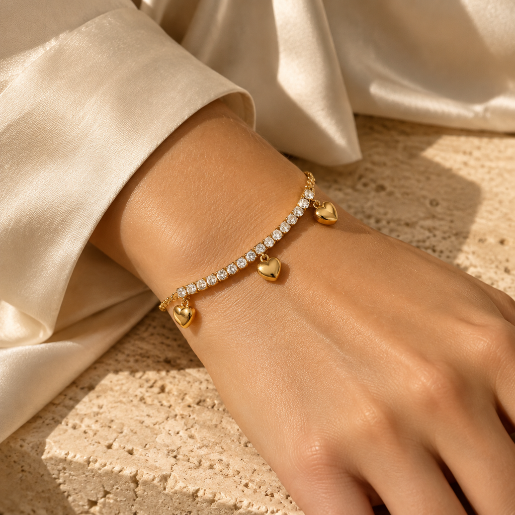 Close-up of a woman's wrist wearing the delicate gold cubic zirconia tennis bracelet accented with three dangling heart pendants.
