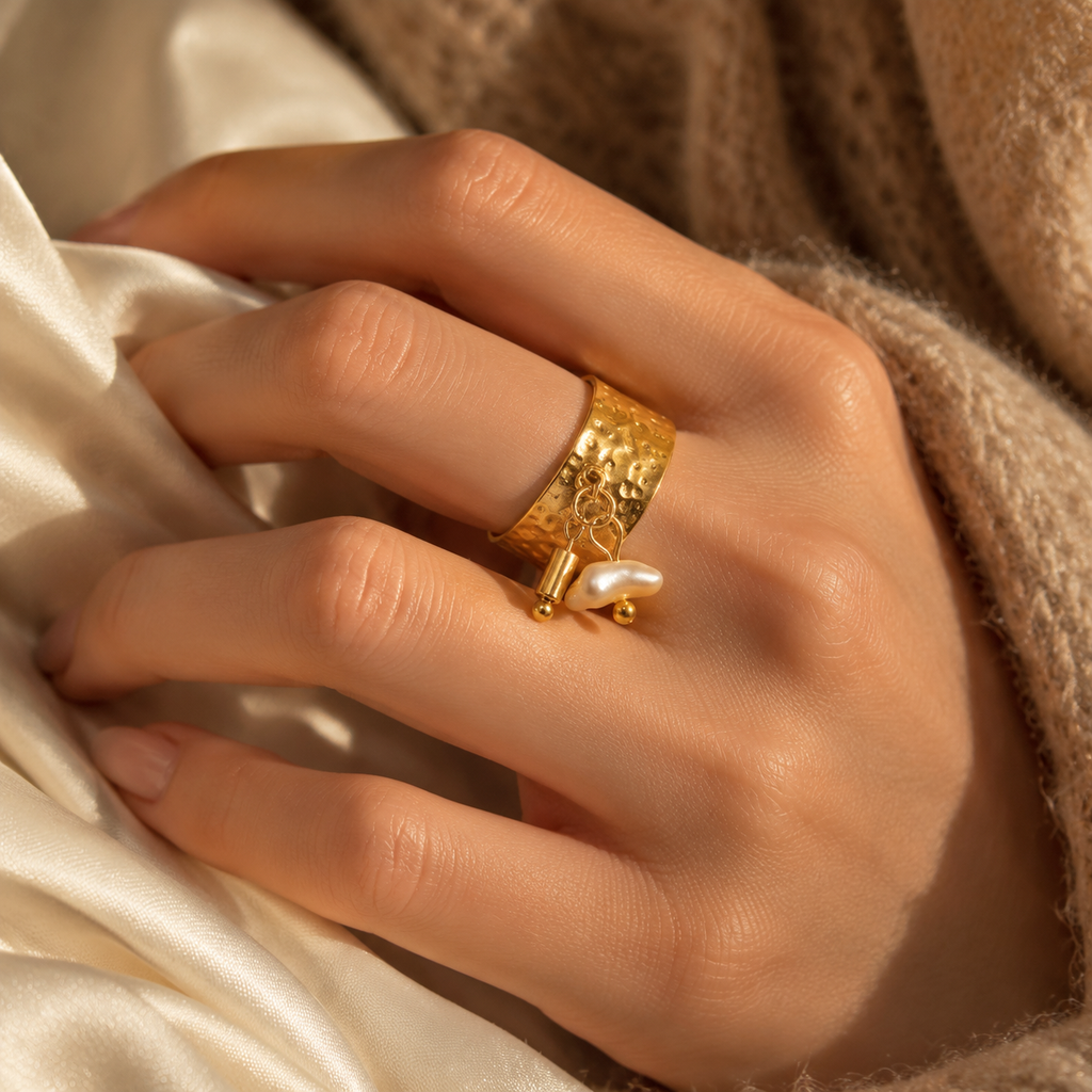 Close-up of woman's hand resting on silk fabric wearing textured gold wide ring with pearl charm
