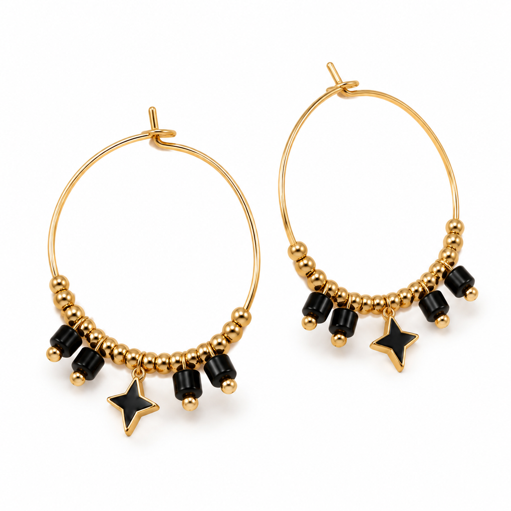 Angled studio shot of two 18K gold plated stainless steel hoop earrings with black accent beads and black enamel star charms
