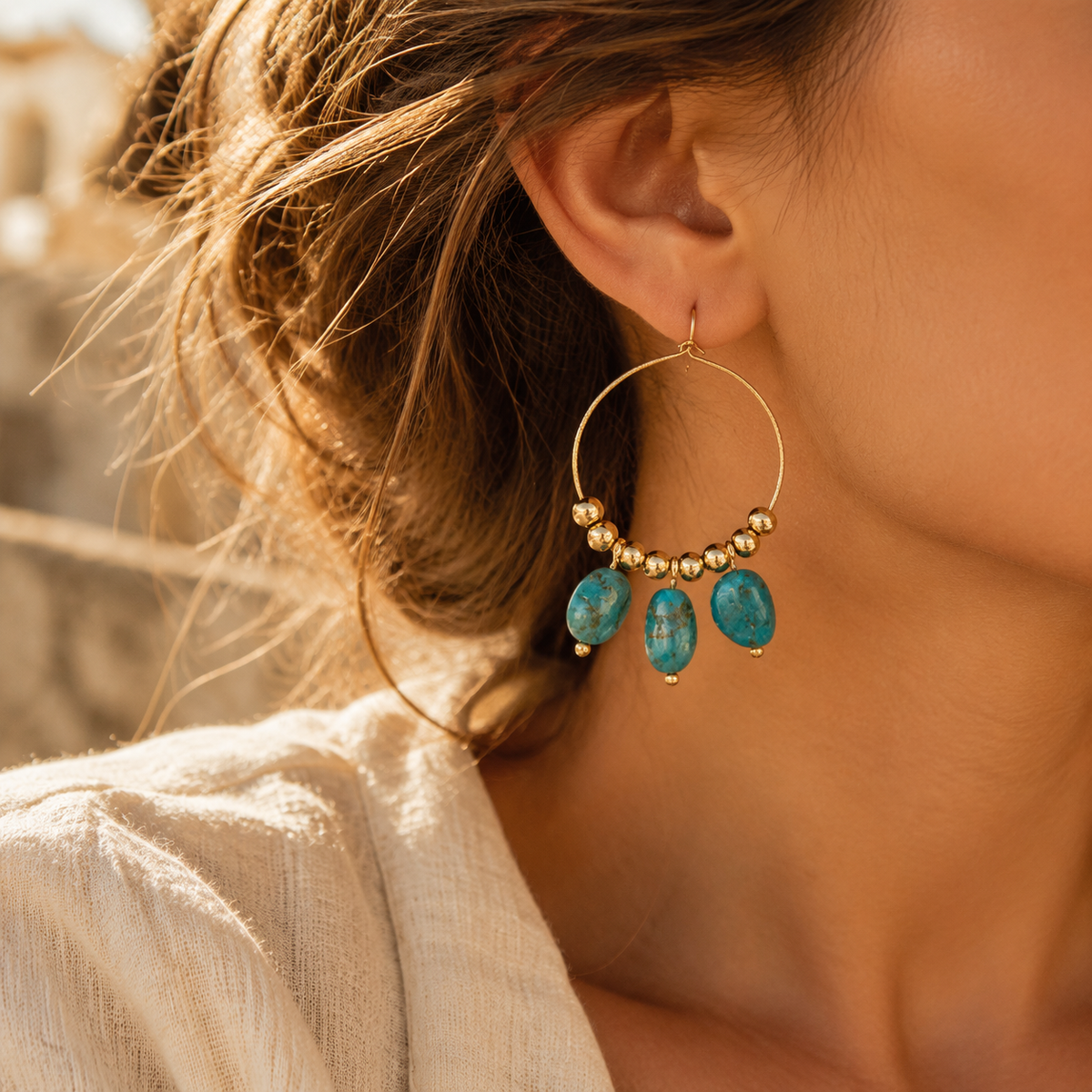 Side profile of woman wearing gold hoop earrings featuring dangling natural turquoise stone nuggets in warm golden sunlight
