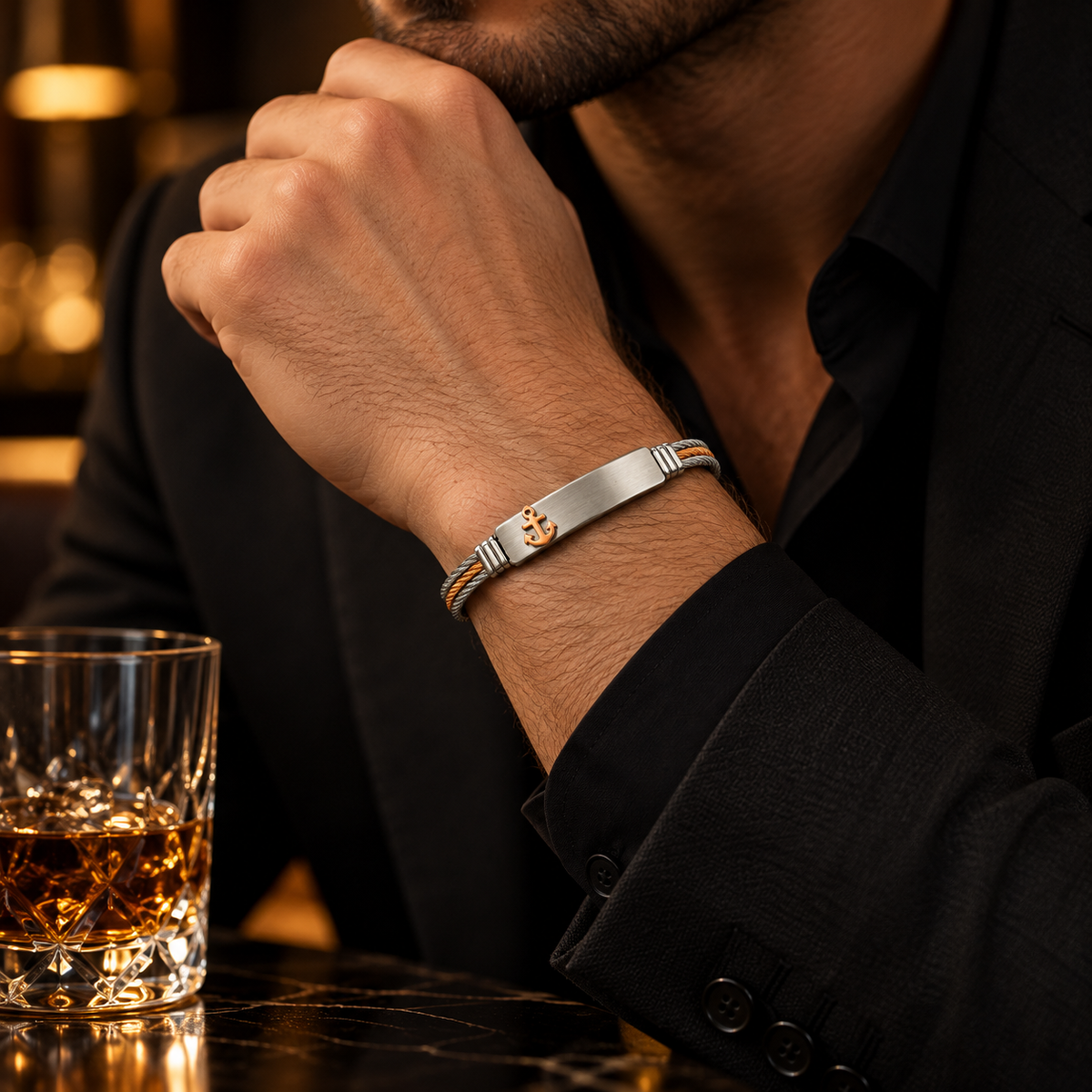 Close-up wrist view of men's cable gold anchor ID bracelet on marble bar table
