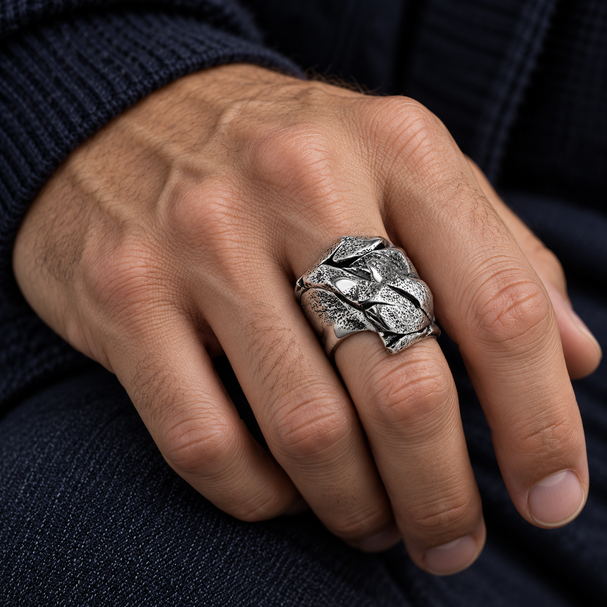Male hand wearing wide textured Cuban link ring resting on dark navy sweater and jeans
