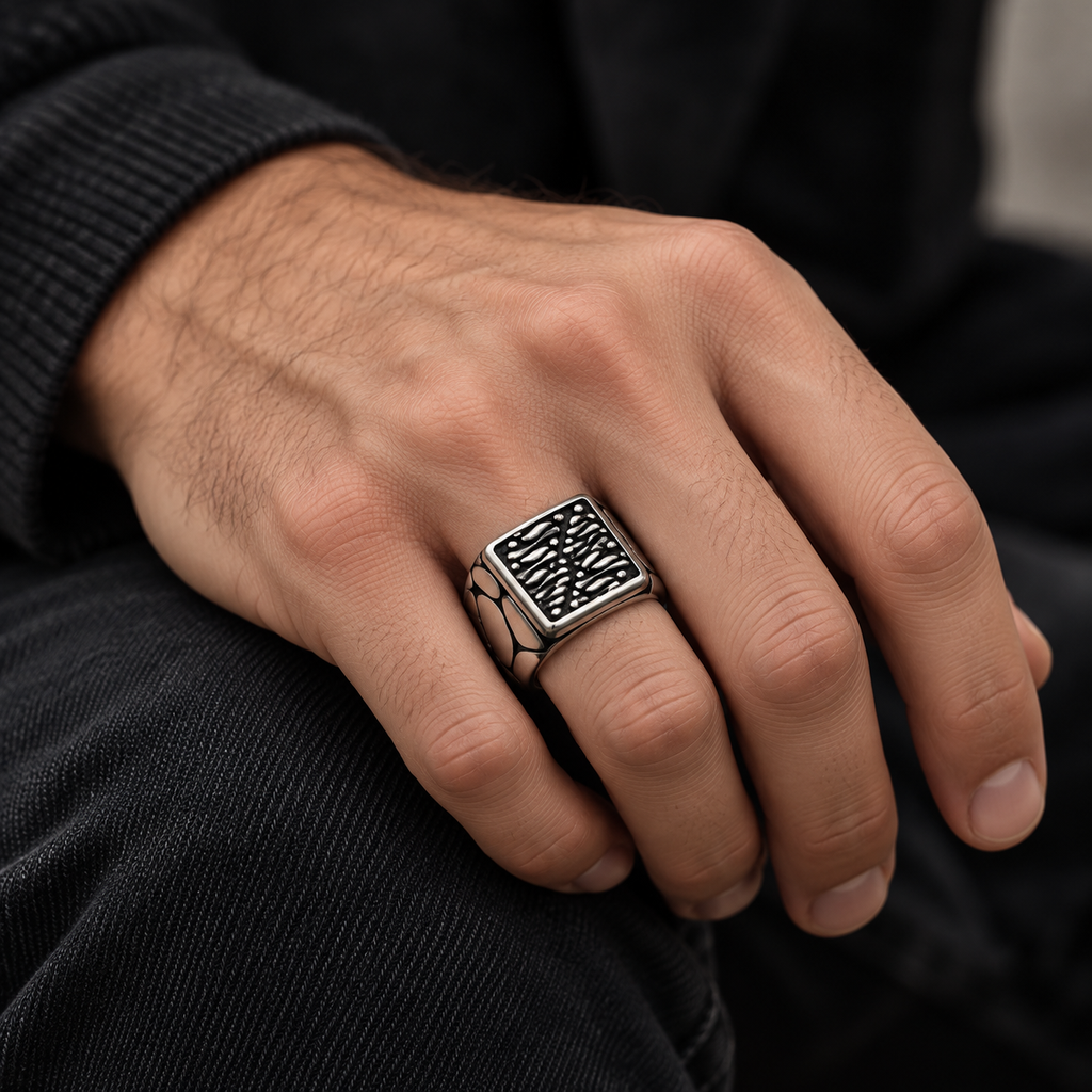 Male hand wearing rectangular textured signet ring paired with black clothing
