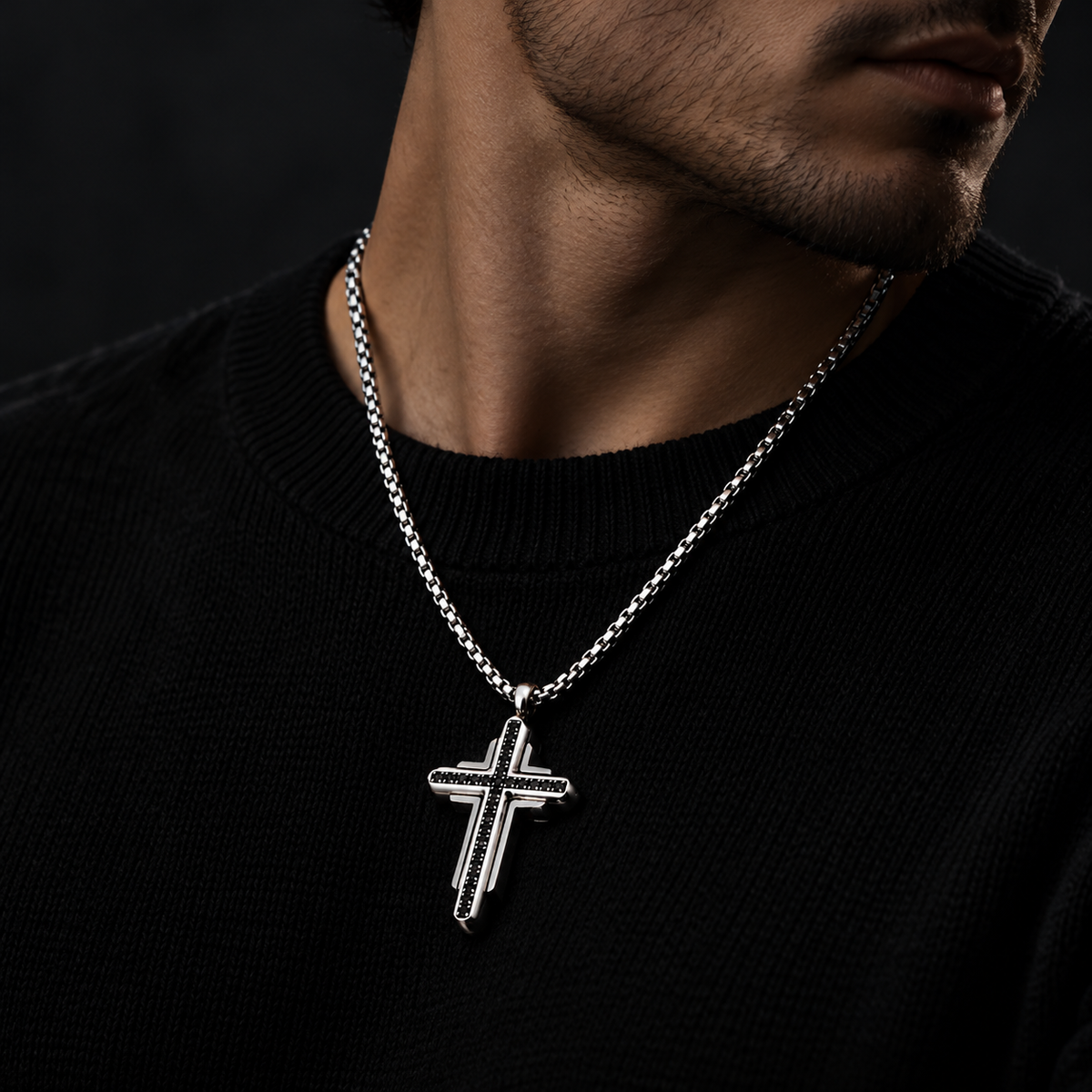 Model wearing men's silver and black stone tiered cross pendant necklace with black crewneck
