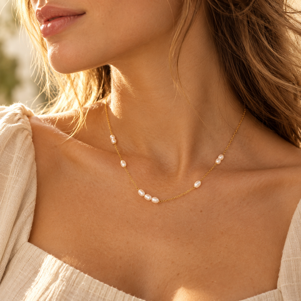 Close-up of model wearing dainty gold freshwater pearl station necklace in golden sunlight
