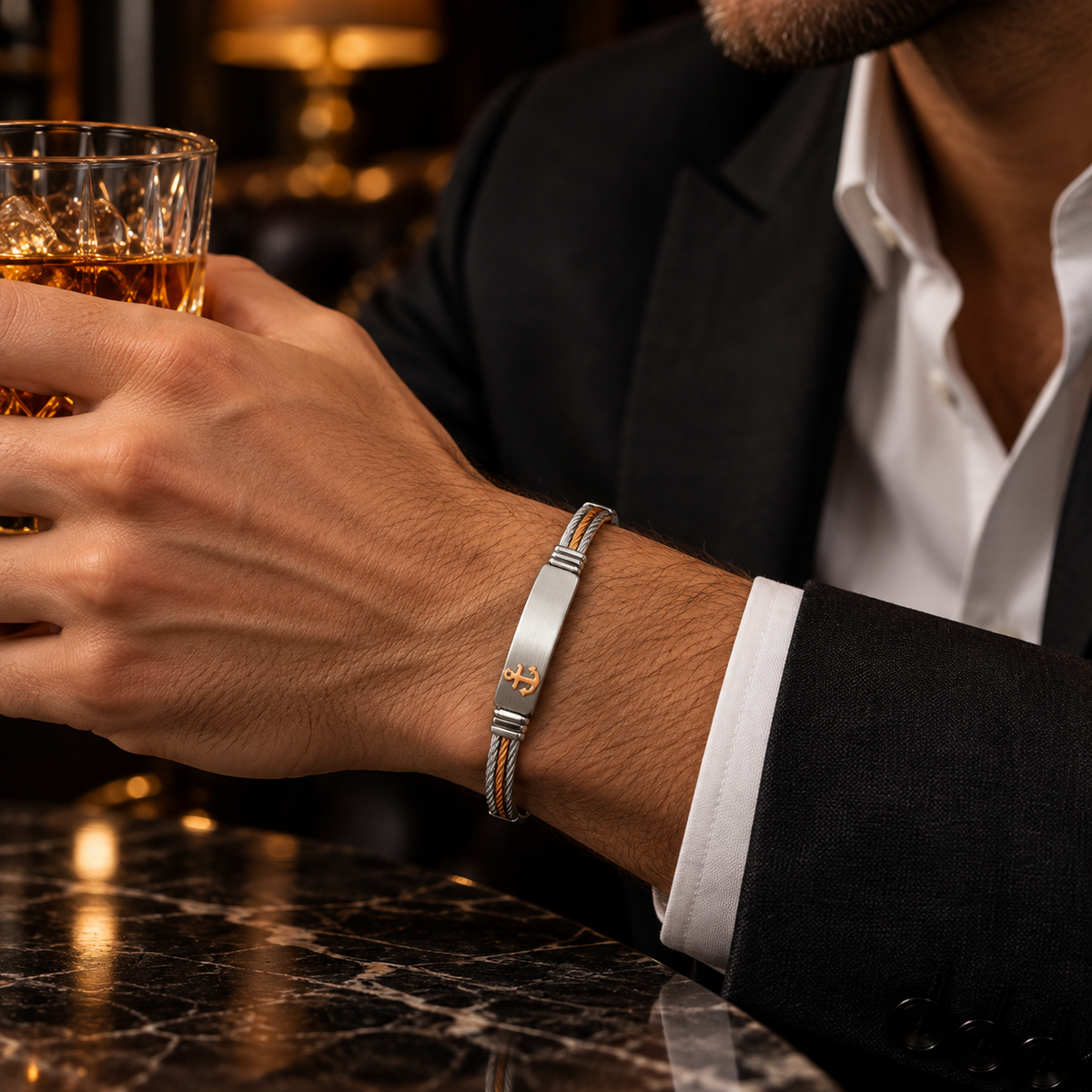 Model wearing men's two-tone wire cable anchor bracelet holding whiskey glass in suit
