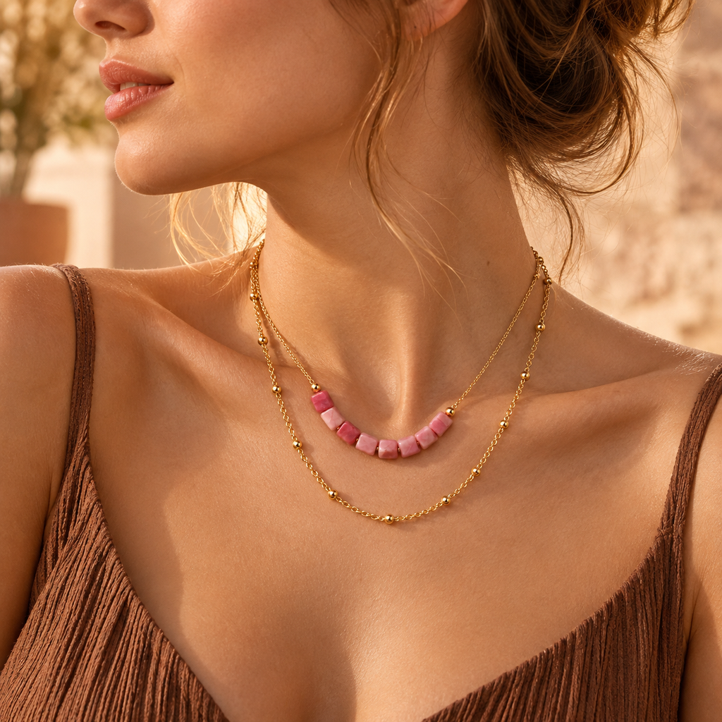 Lifestyle portrait of the layered pink stone bead necklace glistening against a warm bronze dress in natural sunlight.
