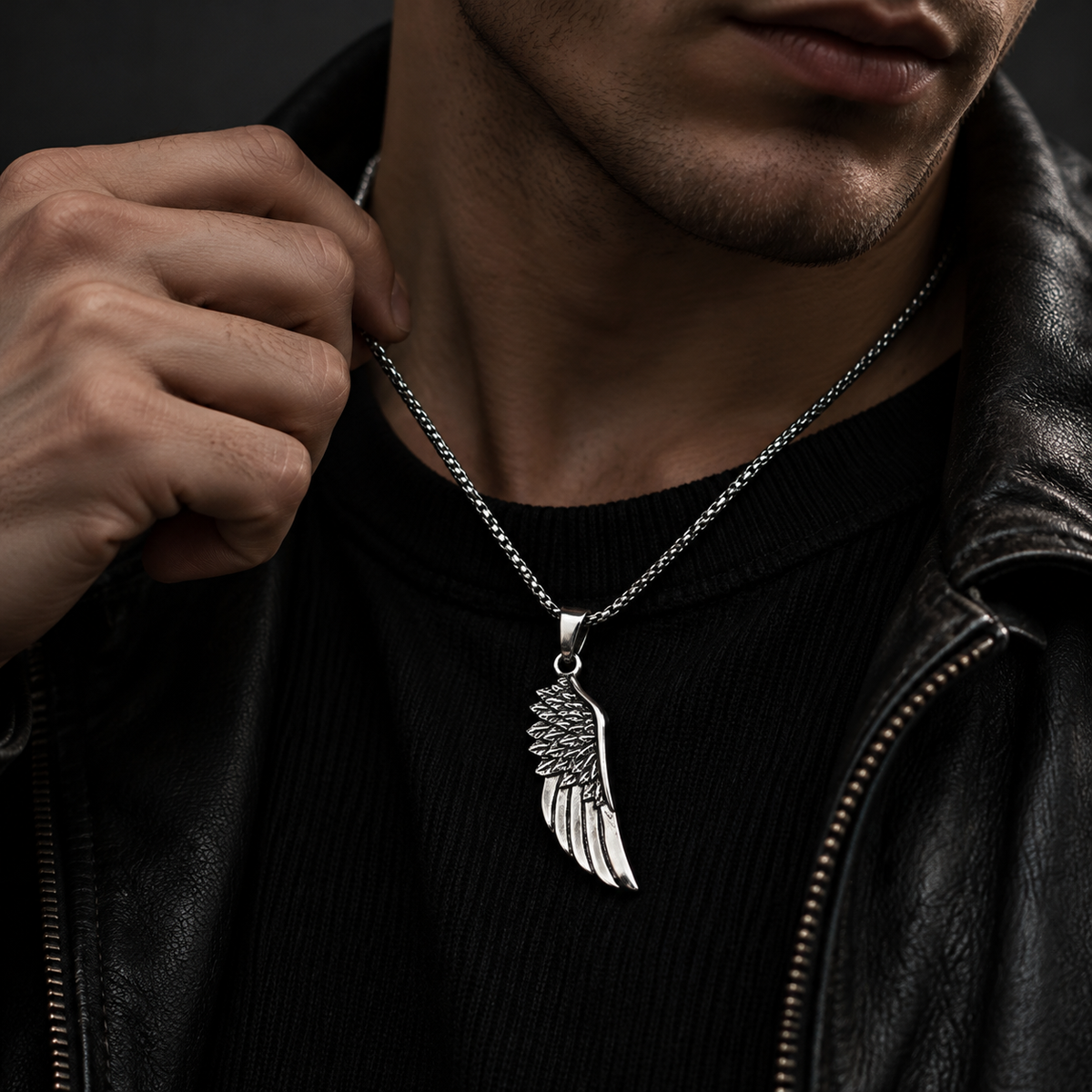 Close-up chest shot of model touching neck wearing men's feathered wing necklace
