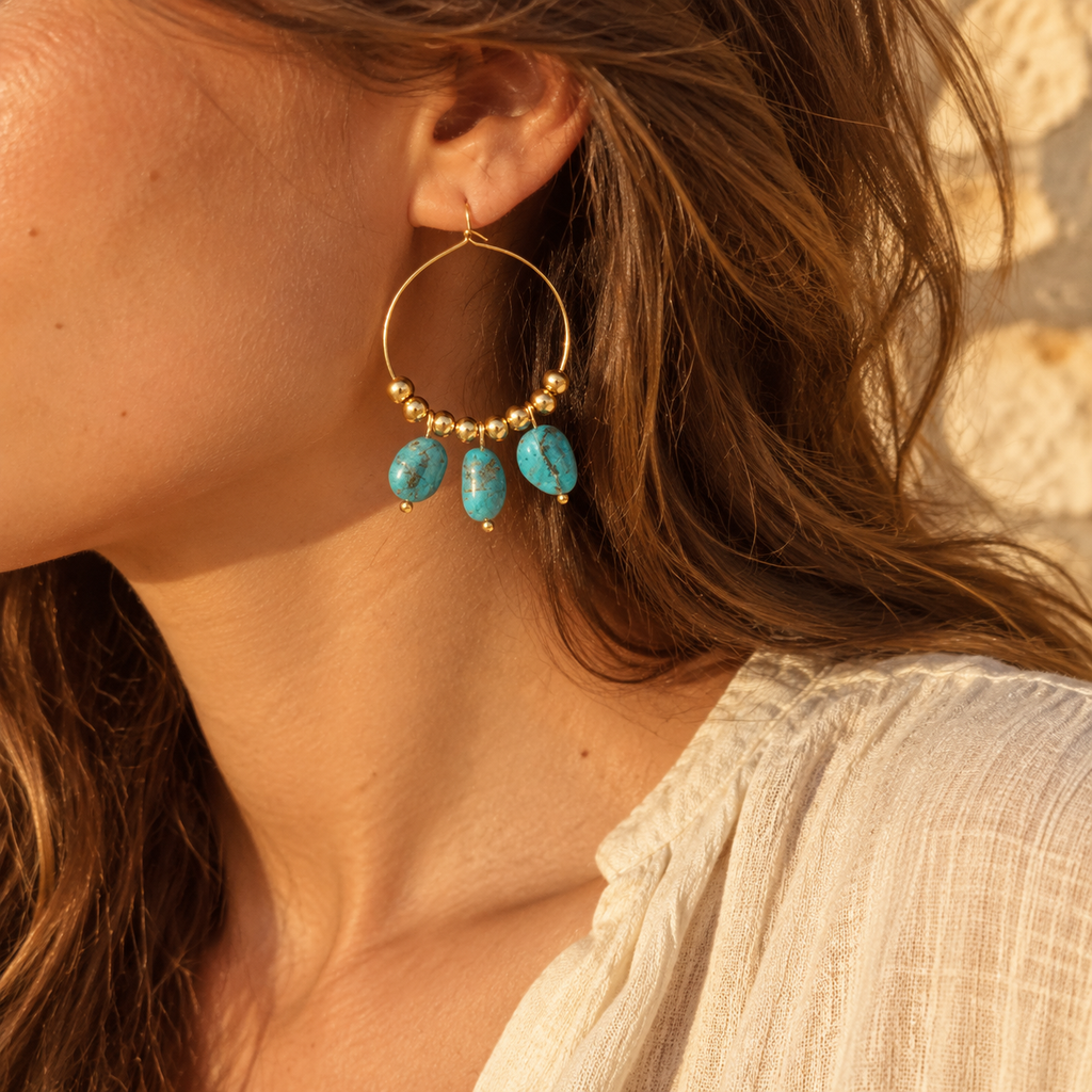 Close-up side view of model wearing bohemian gold beaded hoop earring with turquoise drop stones against rustic stone background
