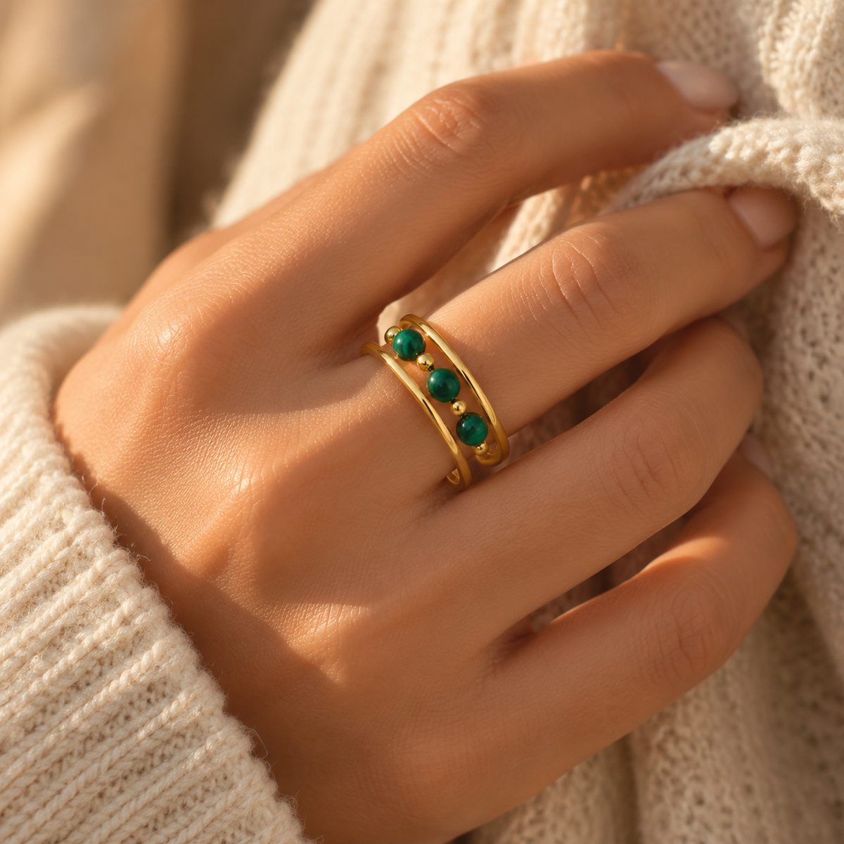 Close-up of woman's finger wearing multi-layer gold ring with green gemstone beads and warm knitwear
