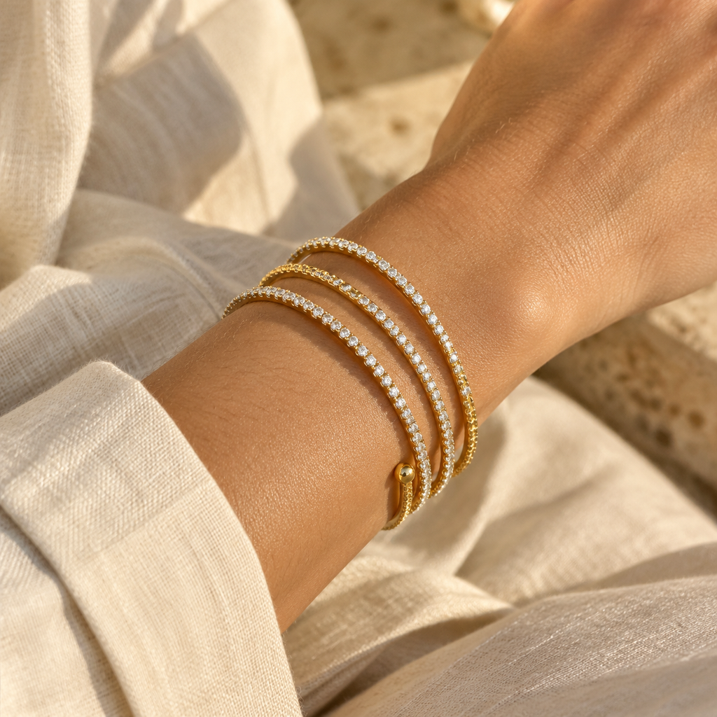 Close-up of a woman's wrist wearing the triple-layer gold spiral CZ tennis wrap bangle bracelet paired with an ivory linen shirt.
