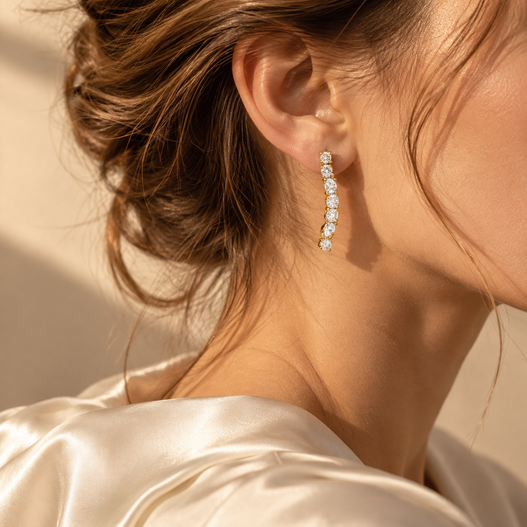 Close-up side view of model wearing elegant 18K gold plated curved crystal tennis drop earrings paired with satin blouse
