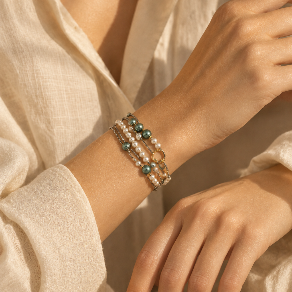 Close-up of a woman's wrist wearing the layered pearl and dark green beaded multi-strand bracelet in warm natural sunlight.
