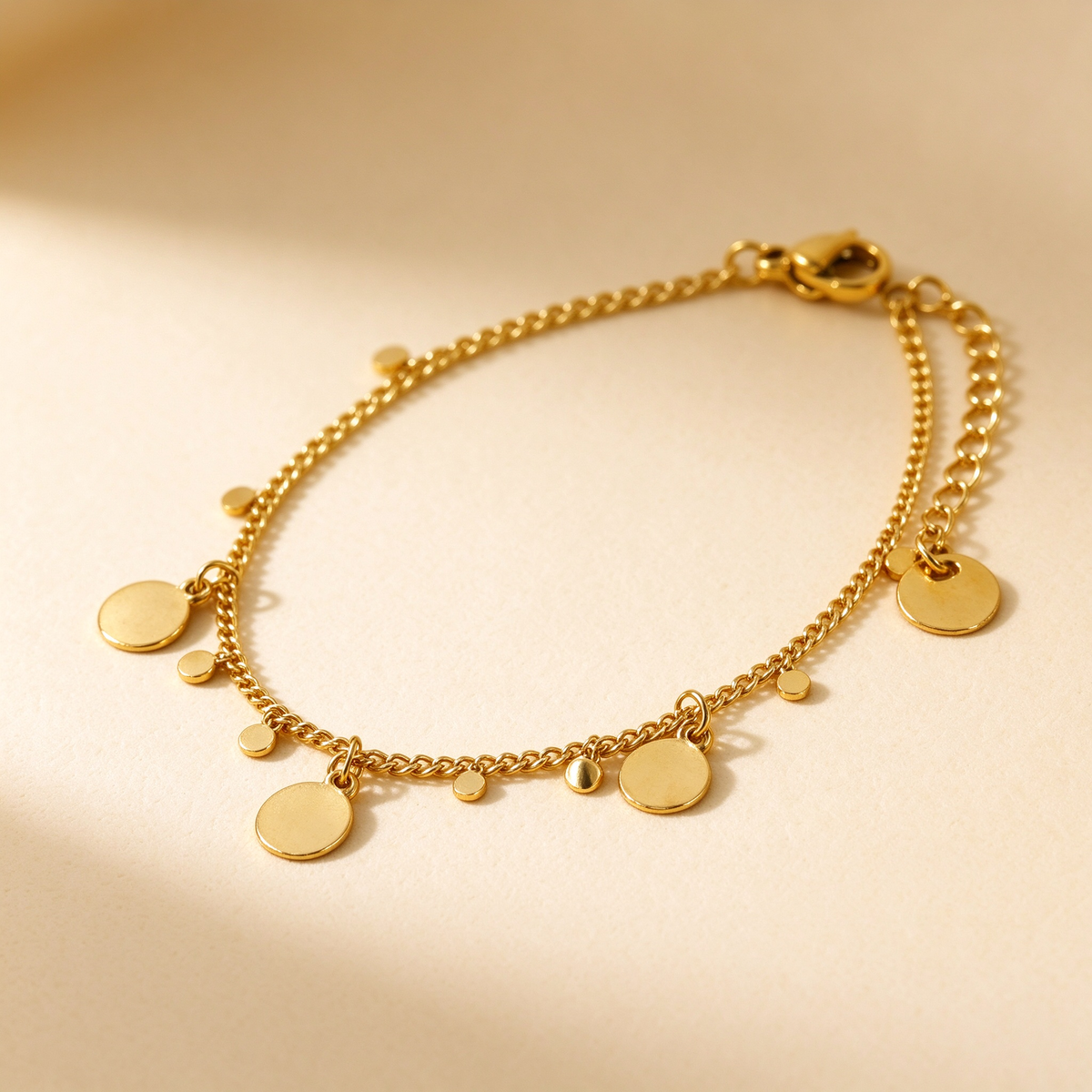 Detailed angled view of women's gold hanging disc charm bracelet on warm background
