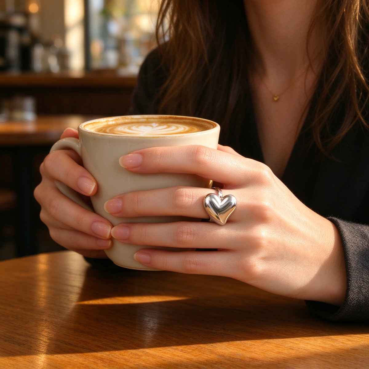 Close-up of woman holding coffee cup wearing bold silver 3D puffy heart statement ring
