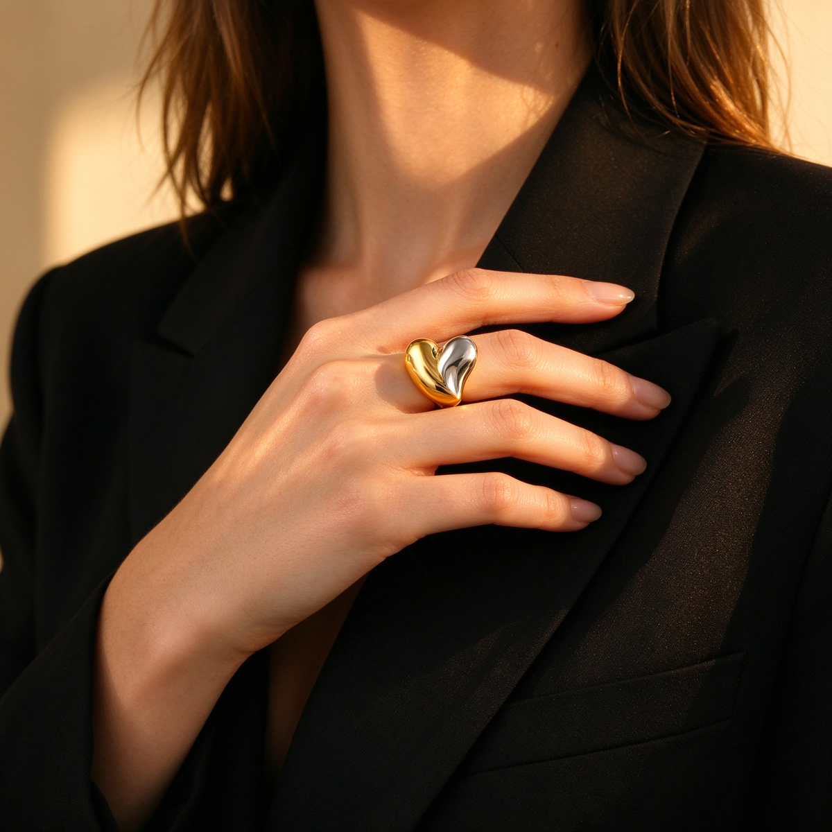 Chic lifestyle shot of woman in tailored black blazer wearing sculptural two-tone heart ring
