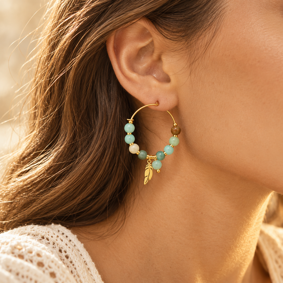 Detailed close-up shot of model ear wearing bohemian natural green beads and gold leaf feather charm hoop earring
