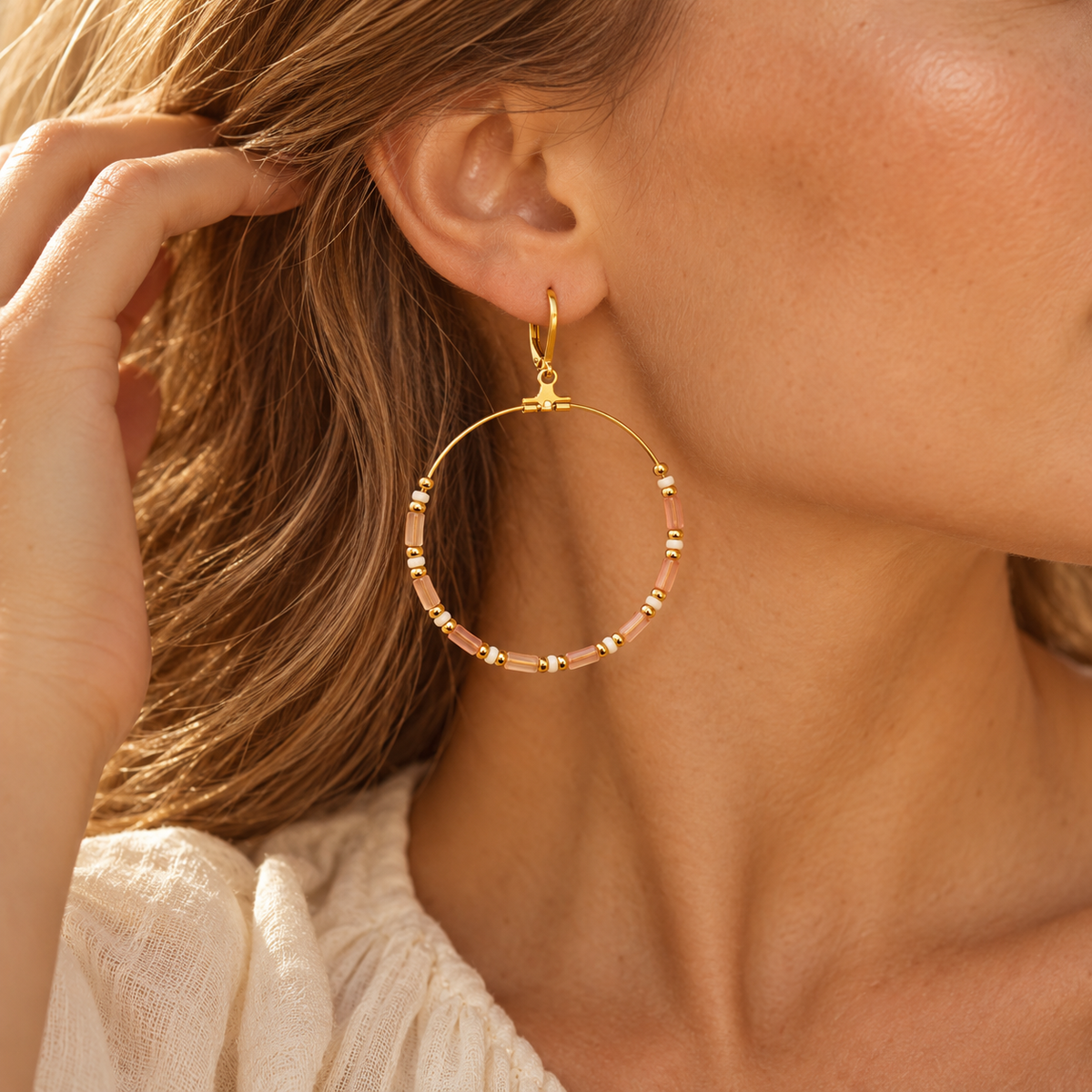 Angled studio shot of two women's gold hoop earrings adorned with pink cylinder beads, white accents, and hinged leverback wires
