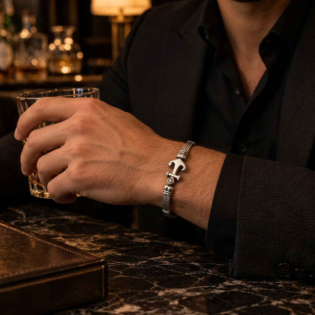 Close-up wrist view of men's cable anchor bangle holding whiskey glass on marble table
