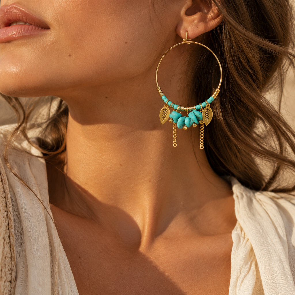 Close-up of model ear showcasing large gold hoop earrings decorated with vibrant turquoise beads and leaf pendants
