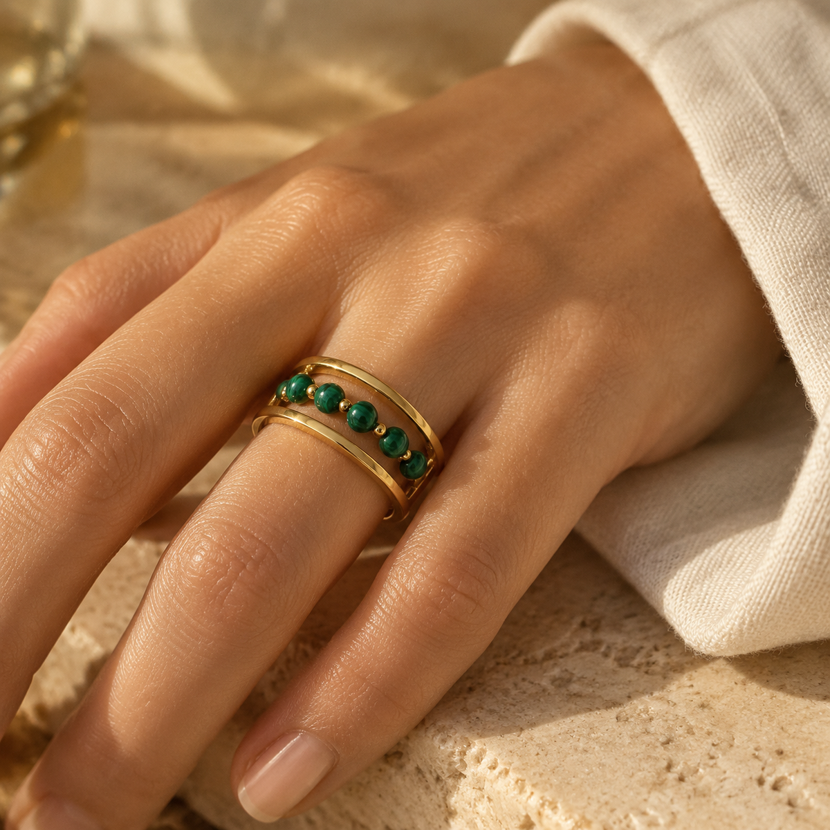 Overhead aesthetic view of woman wearing 18K gold green beaded open cuff statement ring on travertine surface
