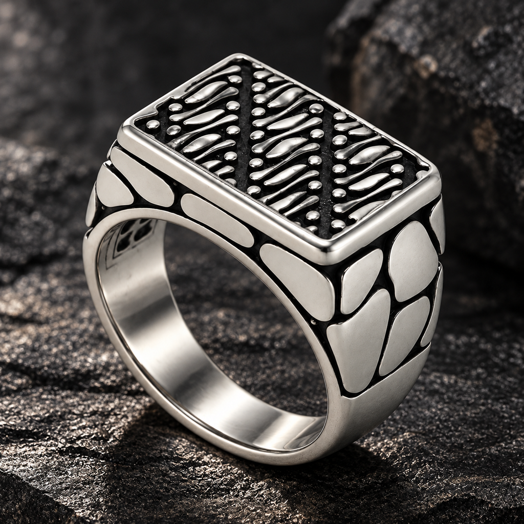 Vintage rectangular stainless steel signet ring displayed on dark volcanic rock
