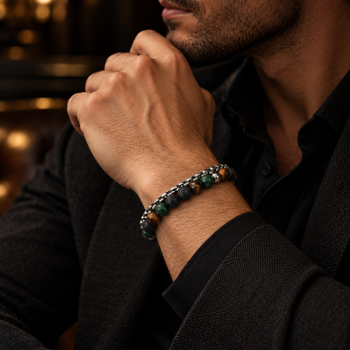 Gentleman in black suit touching chin showing double-layer steel chain and stone bracelet
