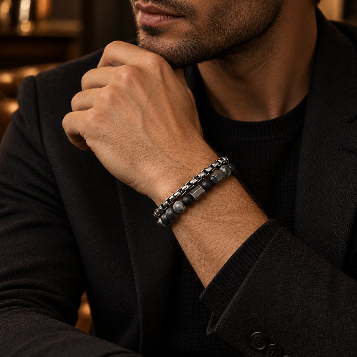 Gentleman in black suit touching chin showing double-strand hematite and chain bracelet
