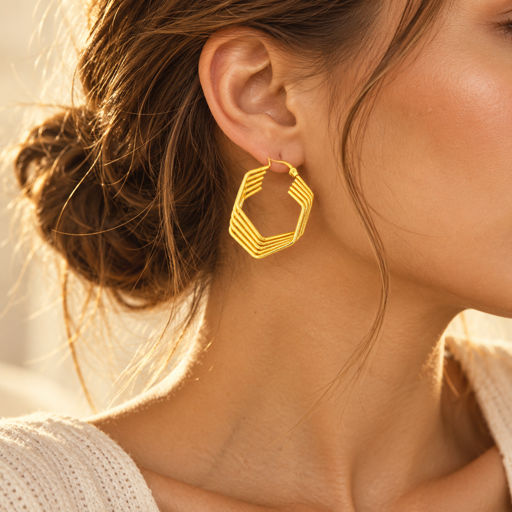 Chic woman styled with architectural gold tiered hexagon hoop earrings and messy hair bun
