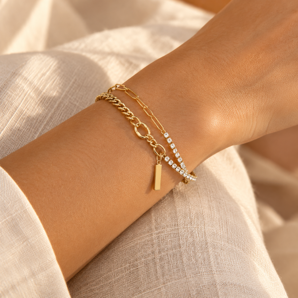 Close-up wrist shot of a woman wearing the layered gold paperclip chain and sparkling rhinestone tennis bracelet with minimalist bar charm.
