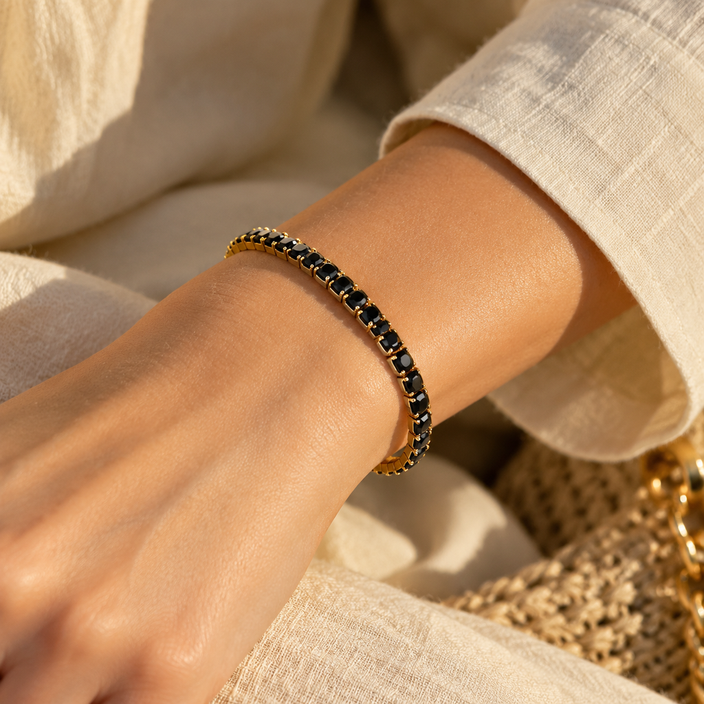 Side profile product flat lay of the flexible gold stretch band tennis bangle showcasing the row of faceted jet black stones.
